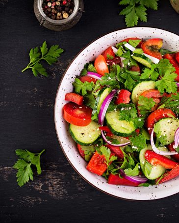 Tomato and cucumber salad with red onion, paprika, black pepper and parsley. Vegan food. Diet menu. Top view. Flat lay